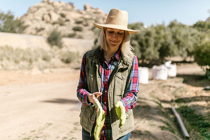 Woman farmer wearing hat and gloves in sunny outdoor setting