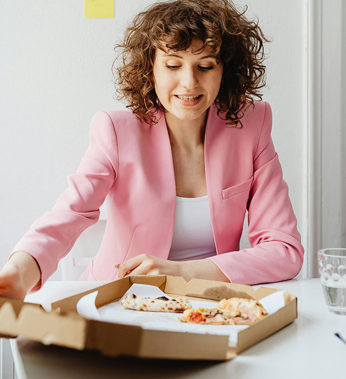 Woman in pink blazer reaching for pizza slice at table