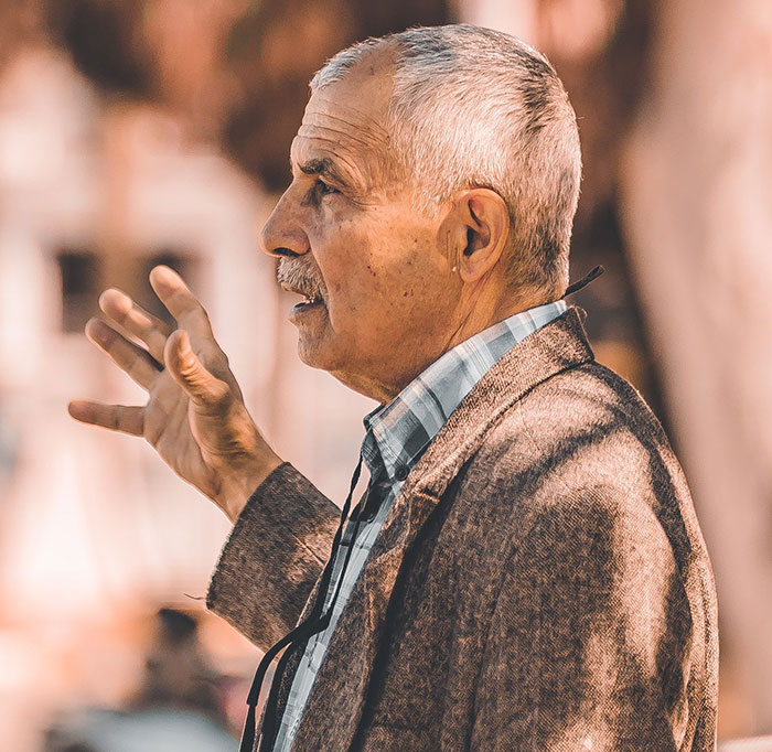Older man gesturing while talking in warm lighting