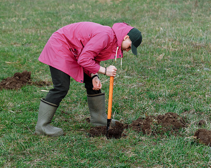 Woman digging soil wearing raincoat and boots outdoor gardening