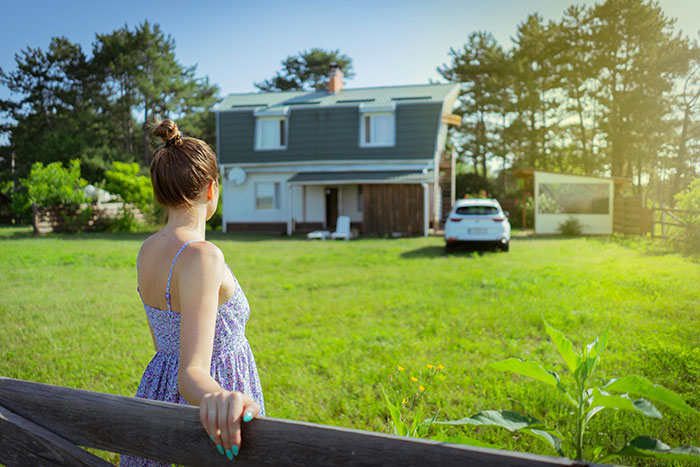 Woman standing outside house with green lawn on sunny day