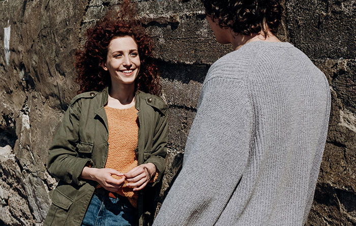 Woman smiling and talking with man outside by stone wall