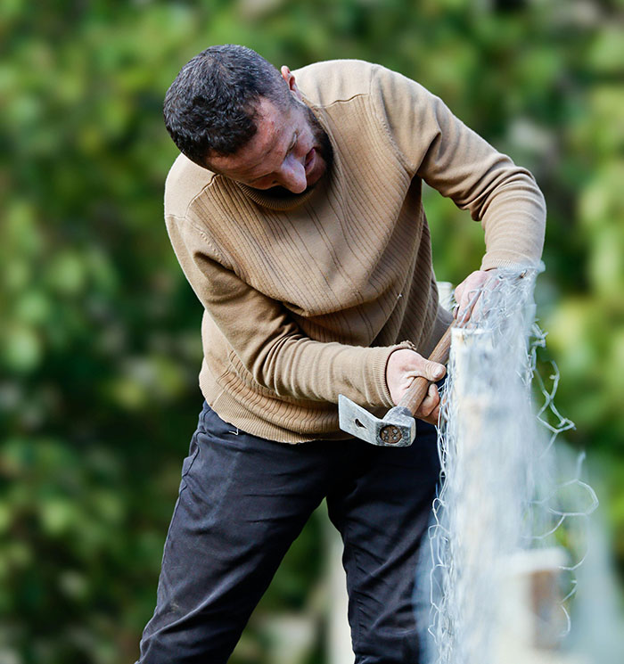 Man fixing wire fence using hammer in outdoor setting