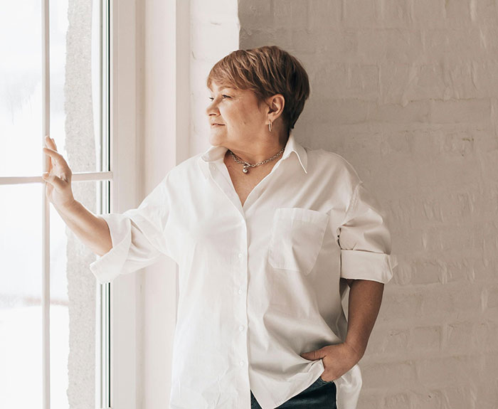 Middle-aged woman looking out window in white shirt, symbolizing free therapist theme