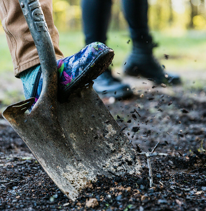 Close-up of foot digging soil with shovel in garden