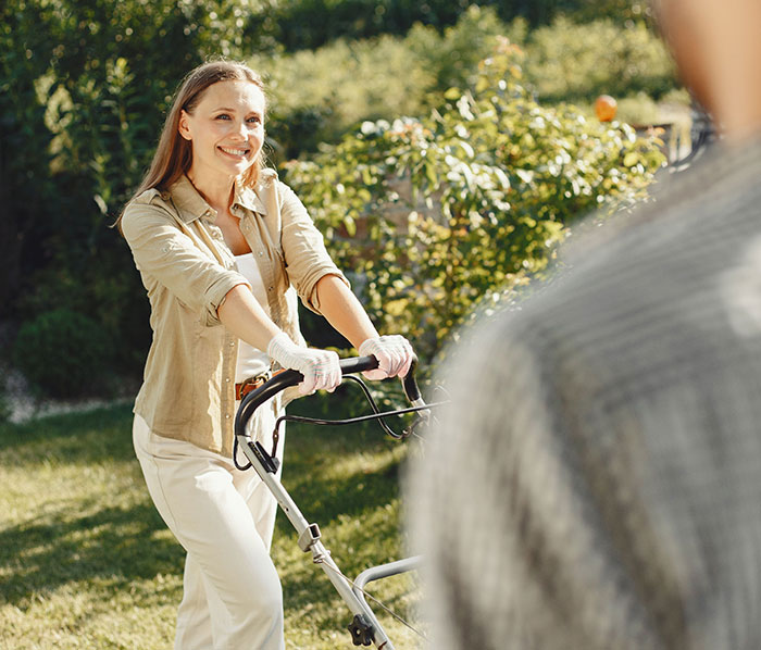 Woman smiling while mowing lawn in garden