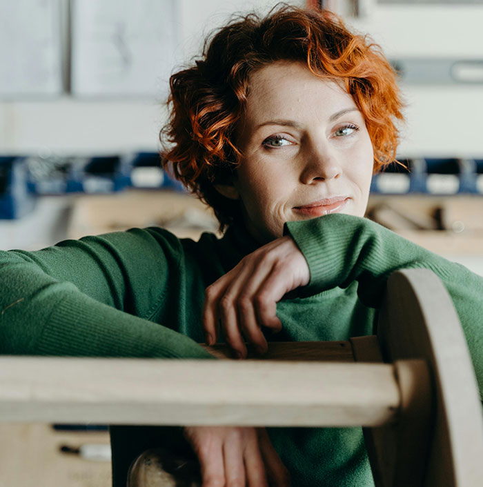 Red-haired woman resting head on wooden chair indoors