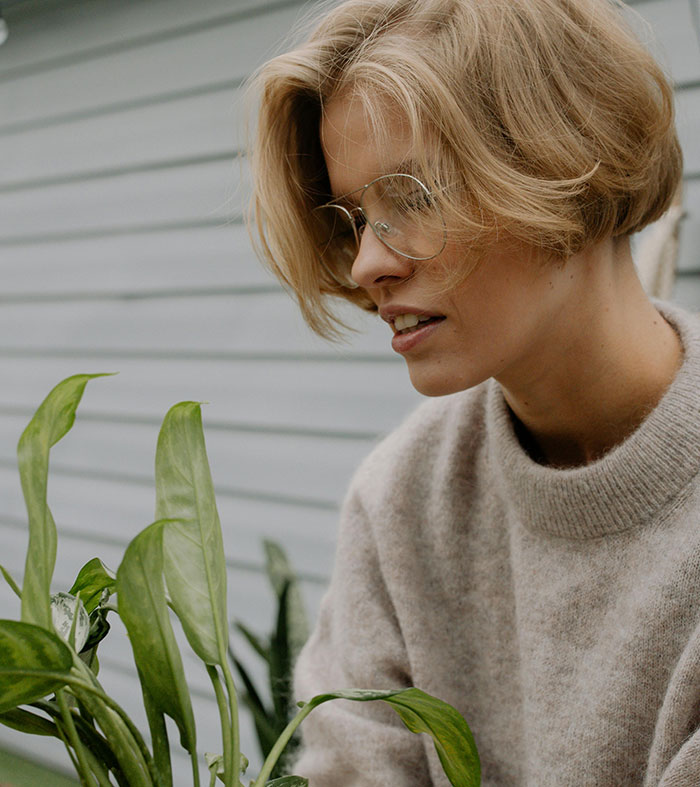 Blonde woman with glasses tending to green plants outdoors