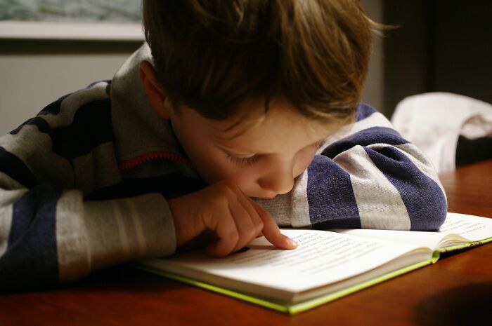 Young boy reading intently from a book at a table