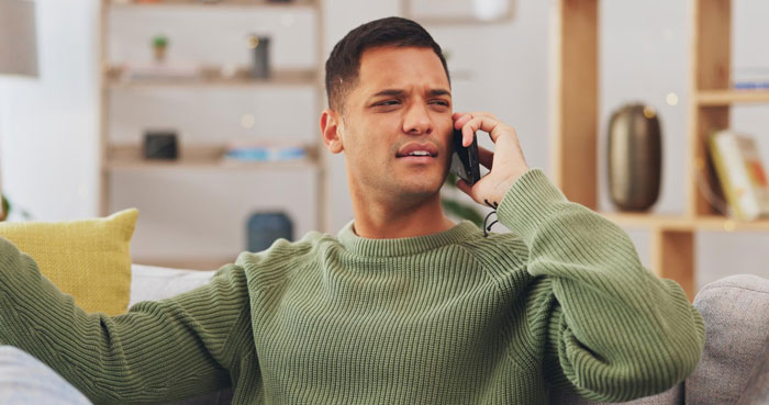 A man with a concerned expression talking on the phone, possibly reacting to MIL wanting final say on baby's name.