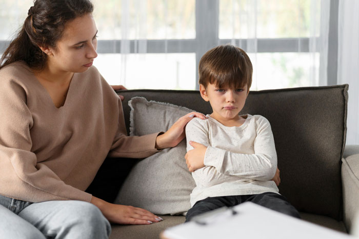 Concerned woman comforting upset boy sitting on couch indoors