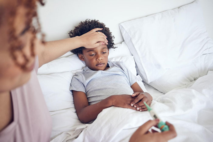 A worried parent checking their son's temperature, who is lying in bed, possibly needing insulin.
