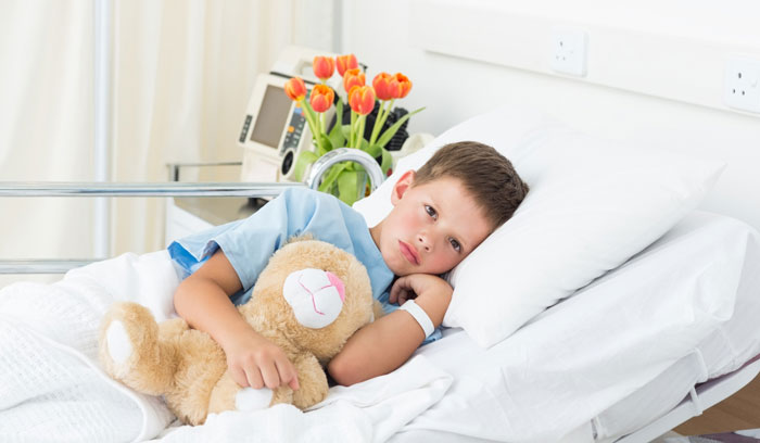 A young boy lies in a hospital bed with a teddy bear, looking ill, after his MIL thought he needed carbs.