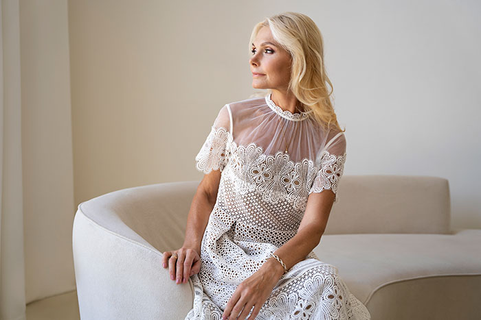A woman in a white lace dress at a son's wedding, possibly the MIL, looking off to the side.