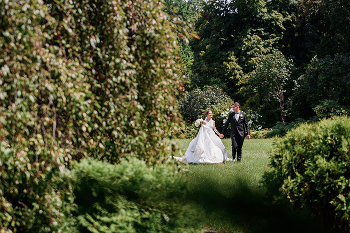 A happy bride and groom walking hand-in-hand through a lush garden at their wedding.