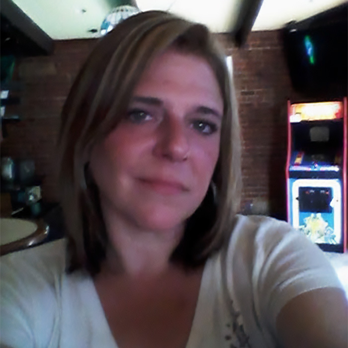 A woman, the mom who goes into the house of horrors, poses for a selfie indoors with an arcade game behind her.