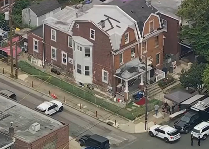 An aerial view of the house of horrors, a residential building surrounded by crime scene tape and police vehicles.