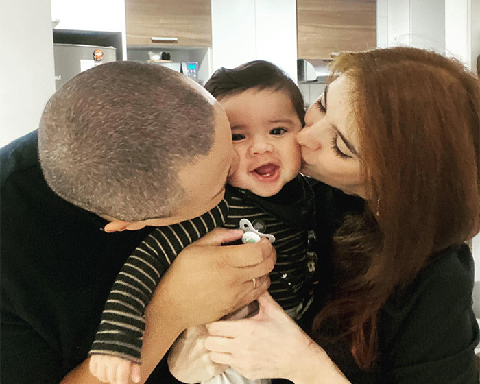 A mom and dad happily kissing their smiling baby on the cheeks, after a mom hid an audio recorder.
