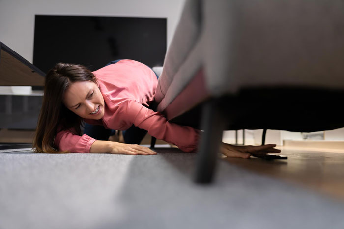 A religious mom snooping in her teen's room, reaching under a sofa with a look of frustration.