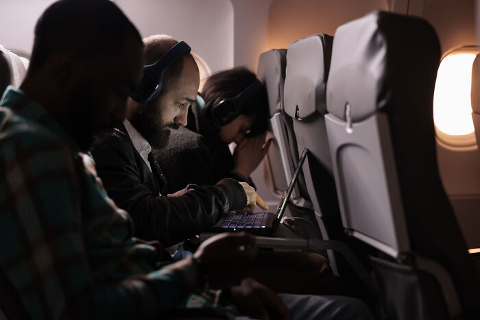Passengers seated on airplane using laptops and headphones during flight