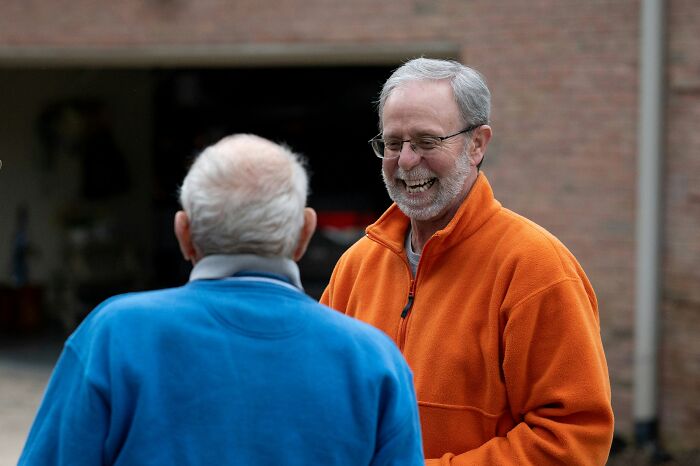Two men laugh outdoors, possibly a moment where someone misread social cues and made things super awkward.
