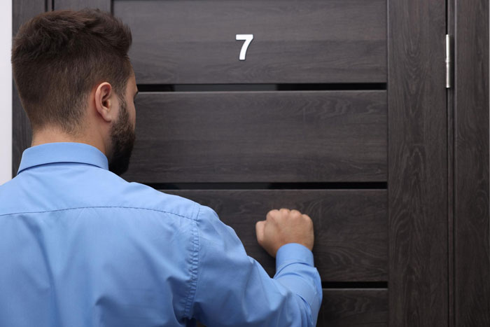 Man in blue shirt knocking on modern dark wooden door numbered 7 Man in blue shirt knocking on modern dark wooden door numbered 7