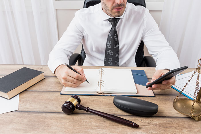 A lawyer at a desk, writing in a notebook and holding a phone, handling neighbor's petty acts case. Revenge for rose garden.