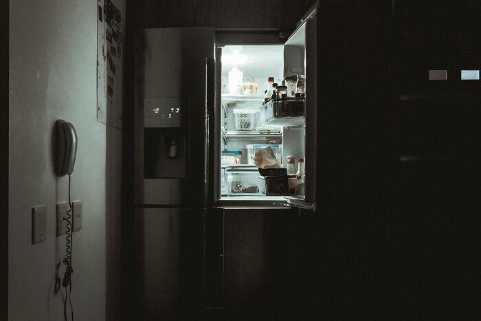 Open refrigerator glowing in dark kitchen showing food inside