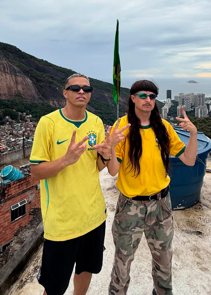 Two men in Brazil soccer jerseys posing on a rooftop with Brazilian flag in background Two men in Brazil soccer jerseys posing on a rooftop with Brazilian flag in background
