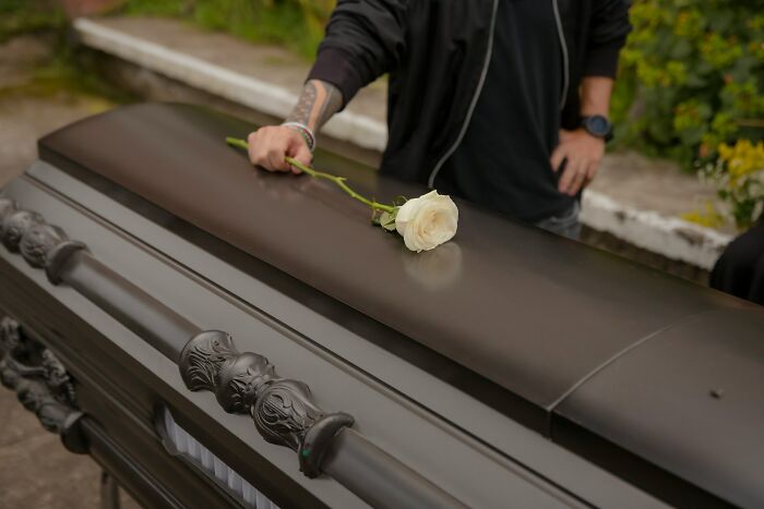 A hand placing a white rose on a dark coffin, depicting an unusual job related to funeral services.