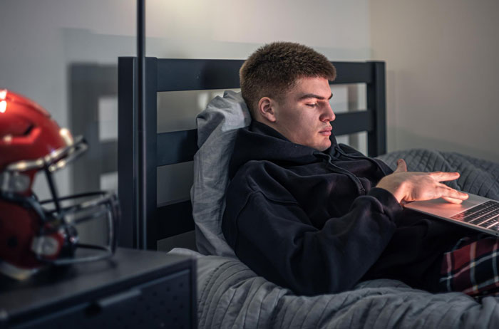 A young man in bed on his laptop, experiencing parents turning hostile and room being given to jobless bro. A young man in bed on his laptop, experiencing parents turning hostile and room being given to jobless bro.
