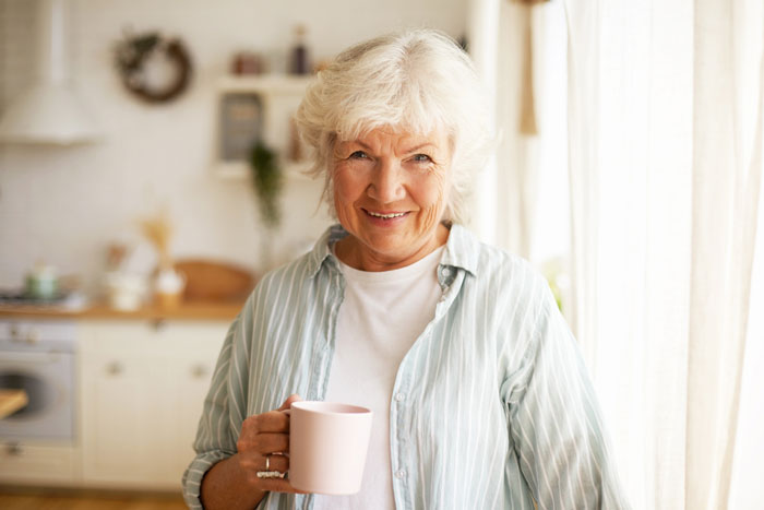 A smiling woman holding a mug, representing the loving parents or grandparents in the story about the 18YO. A smiling woman holding a mug, representing the loving parents or grandparents in the story about the 18YO.