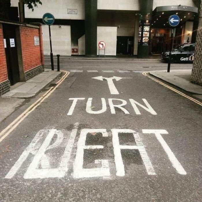 Road with painted arrows indicating turn left, but the text beneath says TURN RIGHT, a common sense fail.