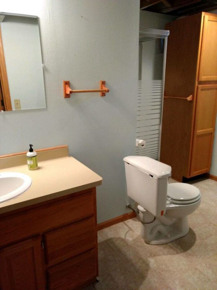 A bathroom with a toilet paper holder installed on the wall too far from the toilet, illustrating a one job fail.