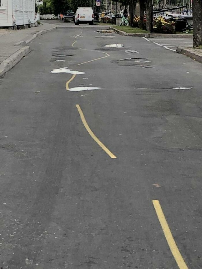 A wavy and broken yellow line painted on a road with potholes, a clear You Had One Job fail.