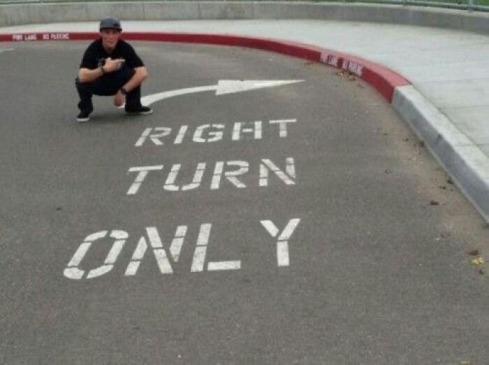 A person crouches next to road markings that say RIGHT TURN ONLY with an arrow pointing left, a funny You Had One Job fail.