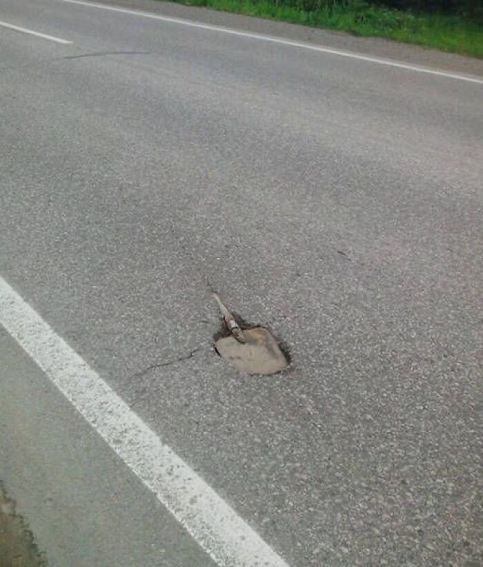 A shovel handle protruding from a pothole in a road, a ridiculous You Had One Job fail that lacks common sense.