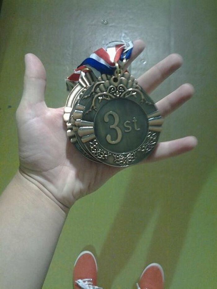 A hand holding a bronze medal that incorrectly reads '3st', showcasing a 'You Had One Job' fail.