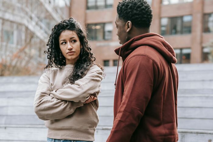A serious-looking woman with curly hair, arms crossed, talking to a man, not a joke for people.