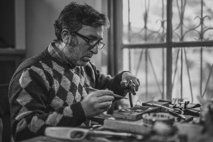 A man working intently at a workbench, with a focused expression, realizing something was not a joke.