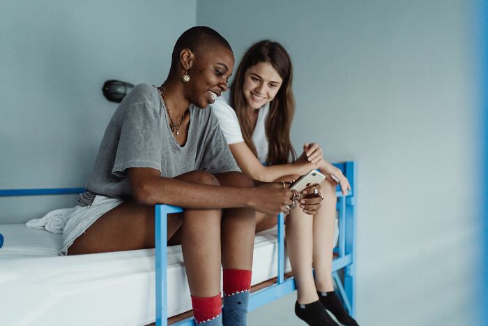 Two women on a bunk bed looking at a phone, realizing something was not a joke.