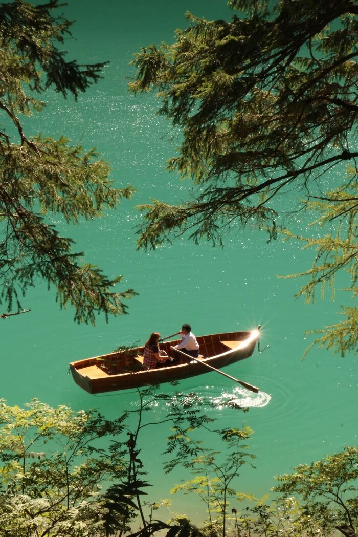 A couple rows a boat on clear blue water, framed by trees, illustrating the wholesome photo trend.