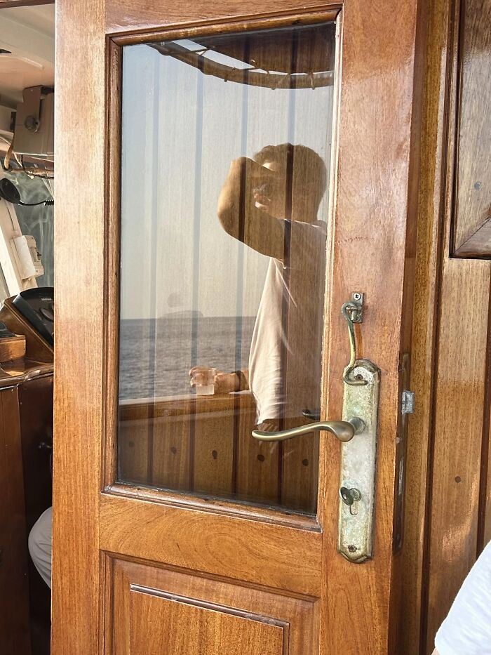 A person is reflected in a glass door with an antique handle, part of the wholesome photo trend.