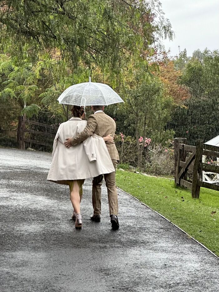 A couple walks away under a clear umbrella in the rain, sharing a wholesome photo trend moment.