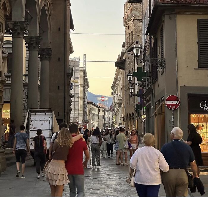 A couple walking down a busy European street with their arms around each other, a wholesome photo trend.