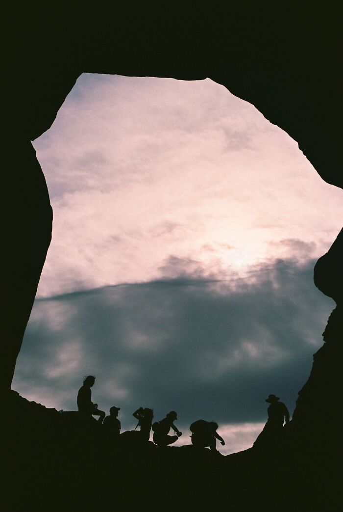 Silhouettes of strangers gathered under a cloudy sky, framed by a rock formation, reflecting the wholesome photo trend.