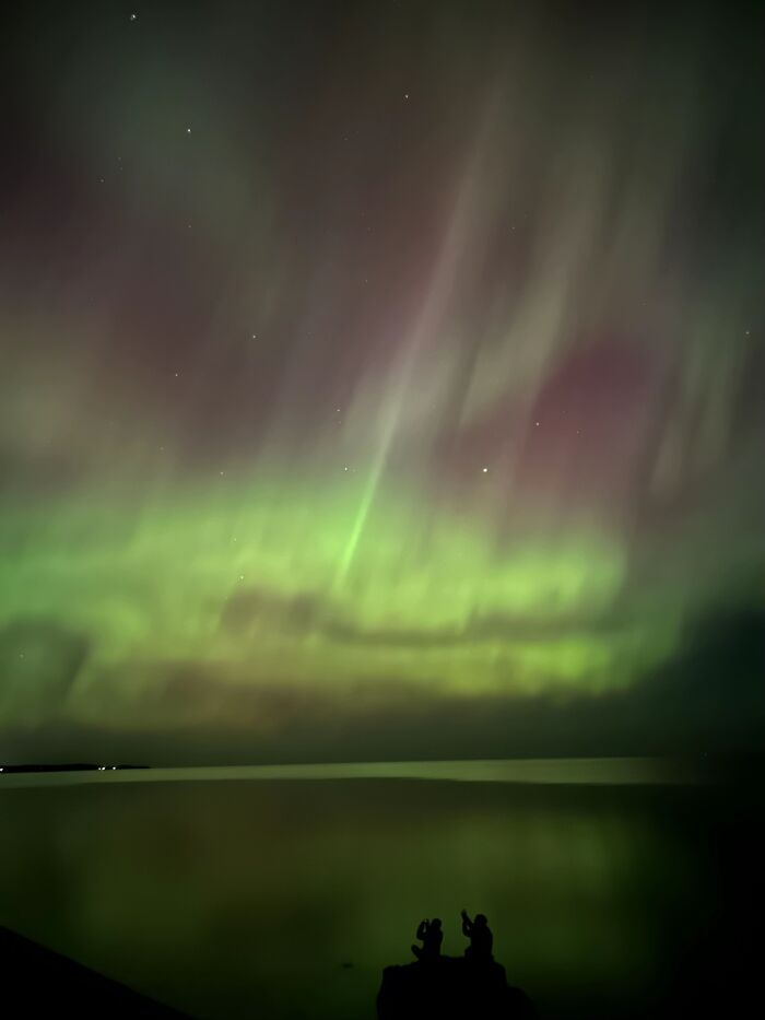Silhouettes of strangers against an aurora, showcasing the wholesome photo trend.