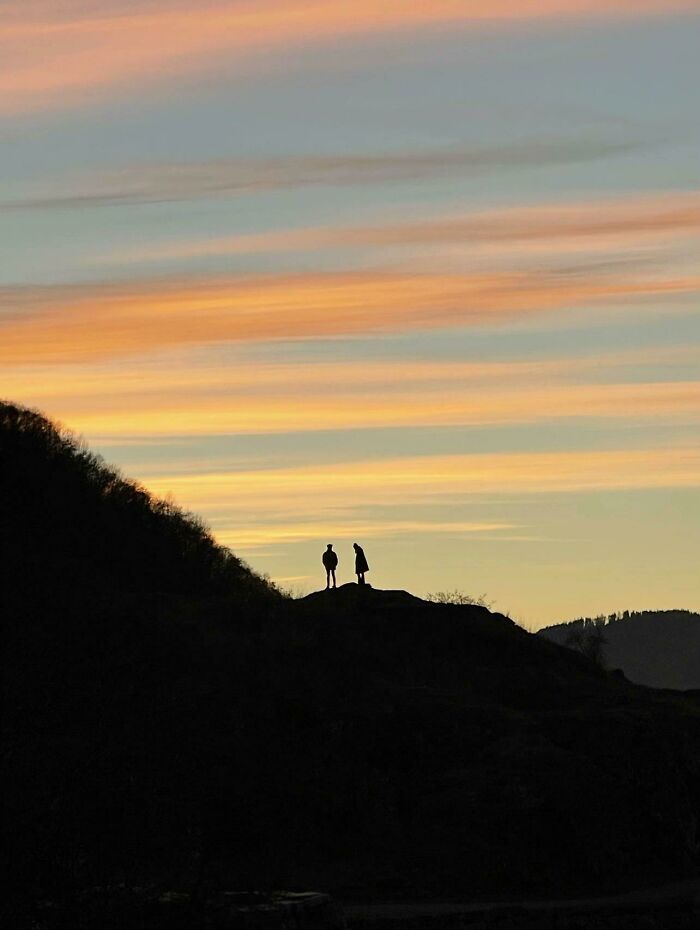 Wholesome photo trend of two strangers silhouetted against a vibrant sunset, like a painting on a hilltop.