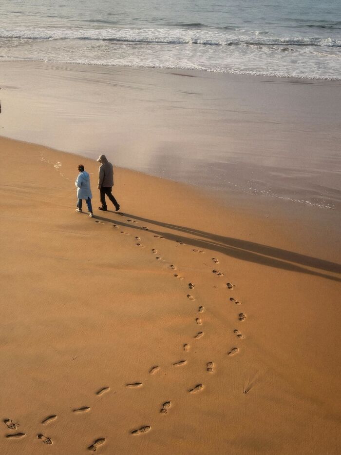 Wholesome photo of two strangers walking on a beach, creating a painting-like scene with long shadows.