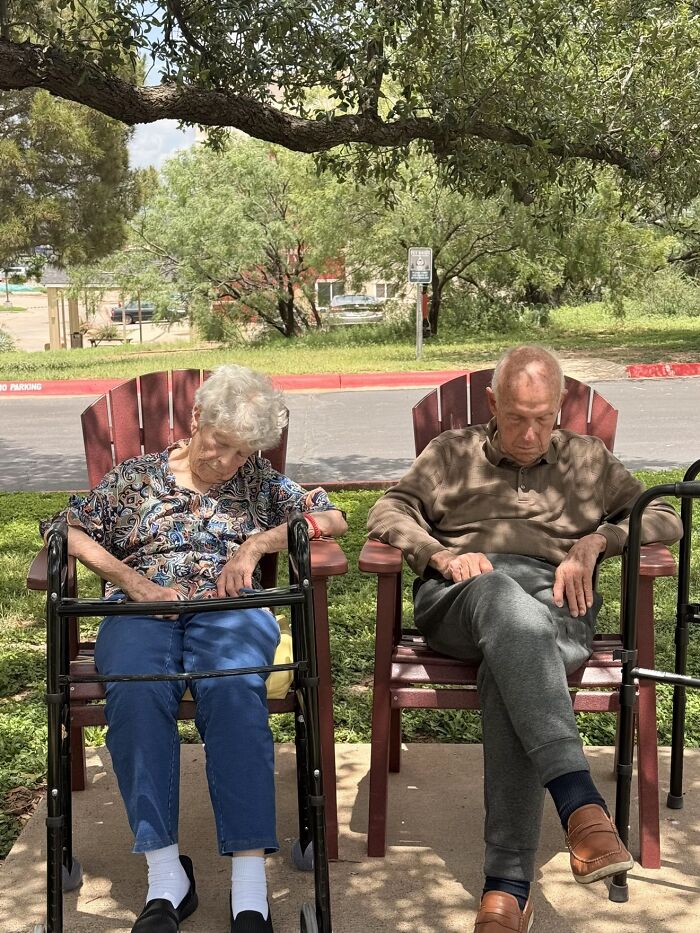 Two elderly people relax in chairs outdoors, seemingly dozing, captured in a wholesome photo trend.